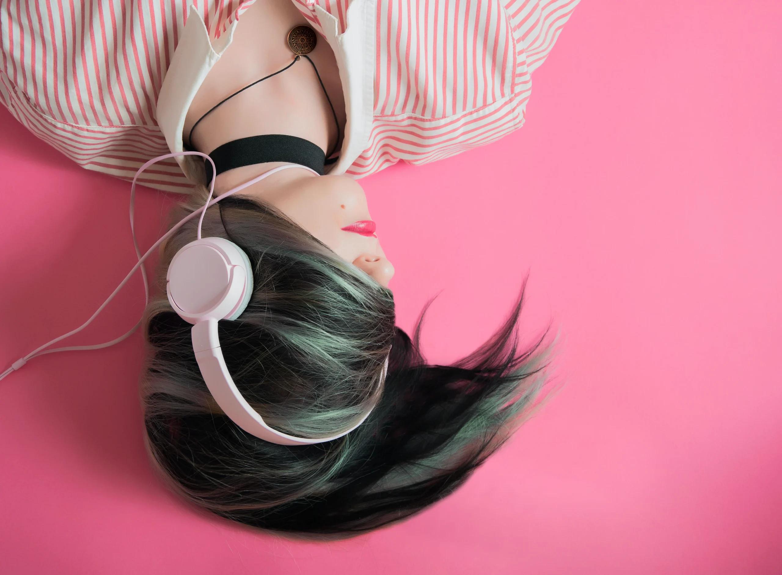 A person listening to music using purple headphones; pink background
