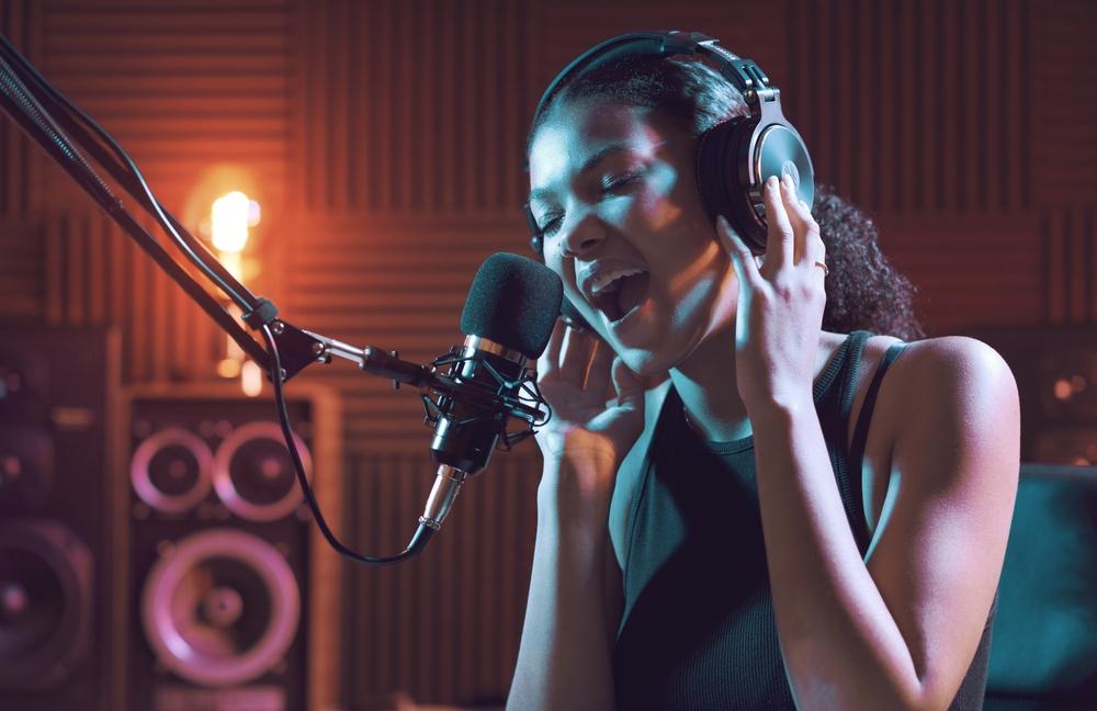 Woman wearing headphones singing into a microphone in a recording studio