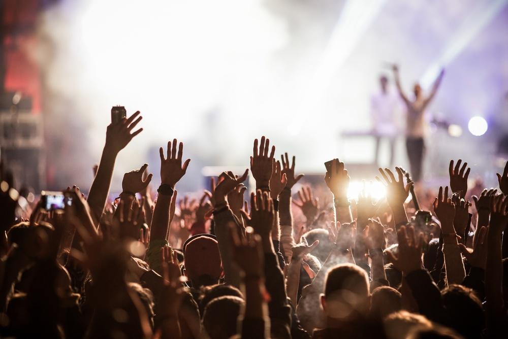 Crowd with raised hands facing a lit stage at a concert